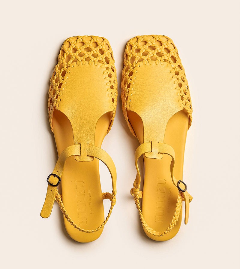 Sandalia plana con entramado trenzado protagonista y cierre con hebilla; el amarillo ámbar se alinea con la paleta “Soft Saffron” destacada para materiales de apariencia natural. Anticipos SERMA | MODA CALZADOS Primavera-Verano 2026/27: Chau Chunky! Bienvenido Slim!